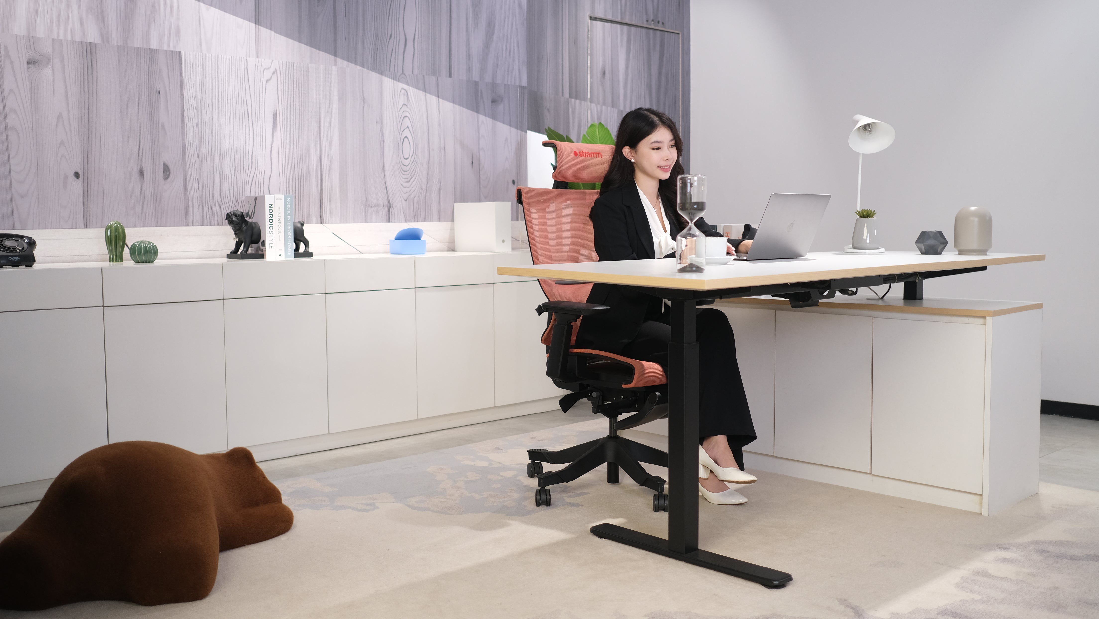 Kursi WFH ergonomis Stramm di ruang kerja modern dengan lazy bear cokelat di atas karpet.