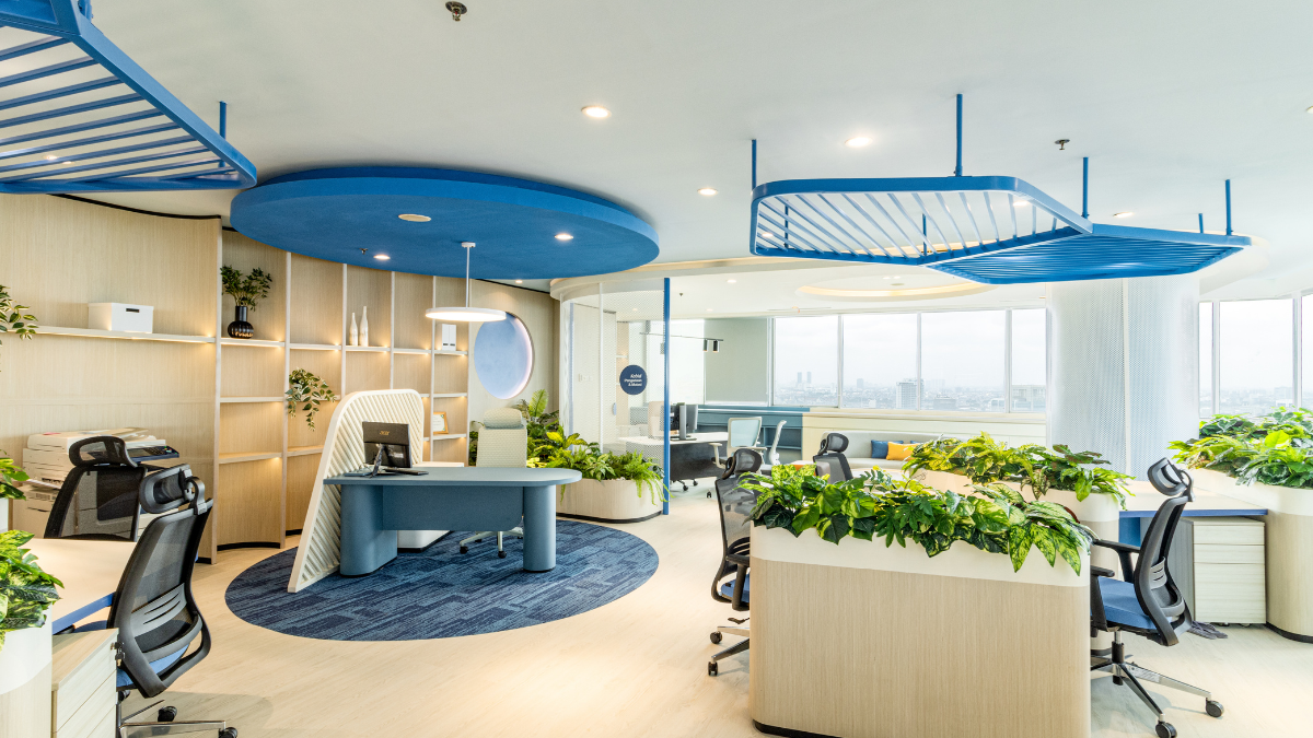 Kursi kantor ergonomis dengan sandaran punggung dan headrest digunakan pada workspace modern dengan desain interior terbuka, meja kerja, serta area kerja yang dipenuhi tanaman hijau.